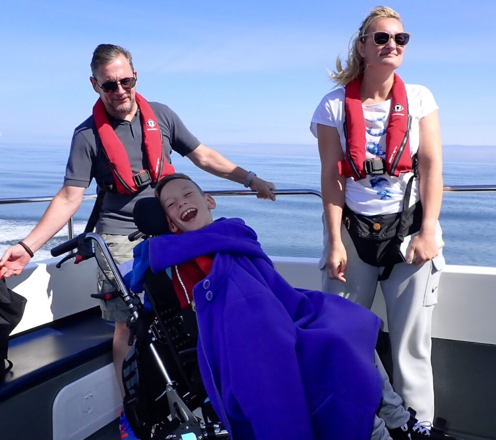 Two adults on a boat with a child in a wheelchair.